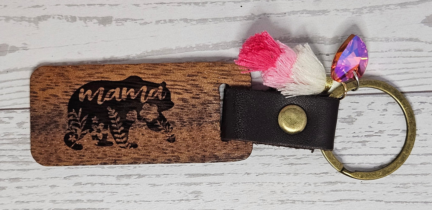 Wooden keychain with leather strap and colorful poms on a light wooden surface